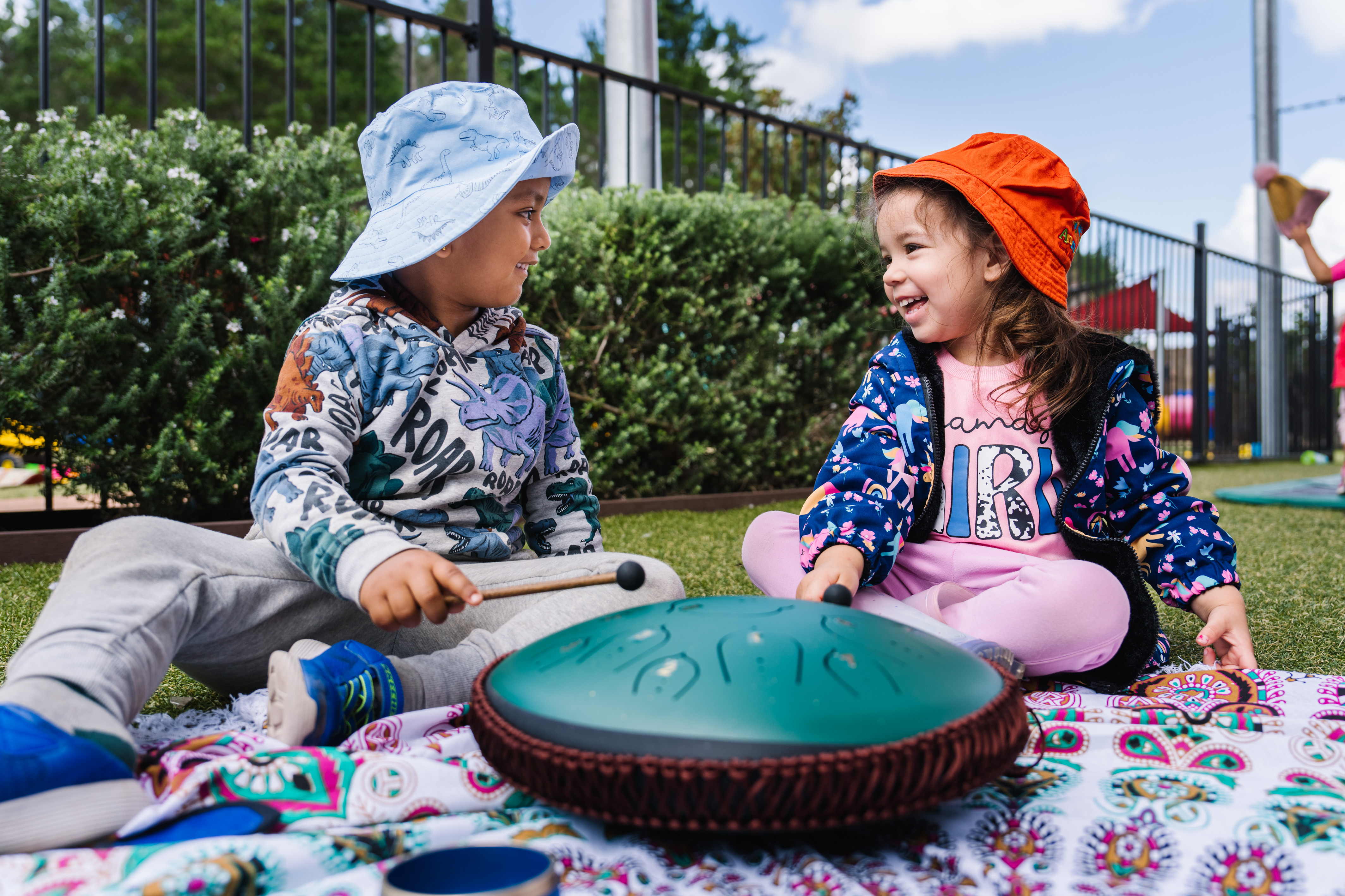 Two children sitting playing a drum